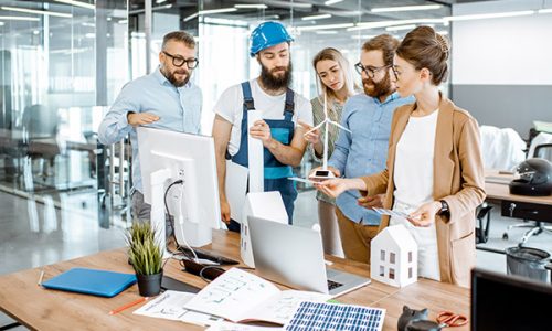 Group of engineers and workman working on a project of alternative energy at the office with computer, wind turbine and solar panels model